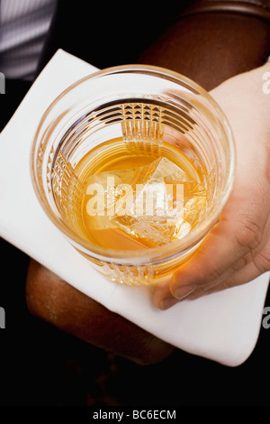 Main tenant un verre de whisky avec glaçons - Banque D'Images