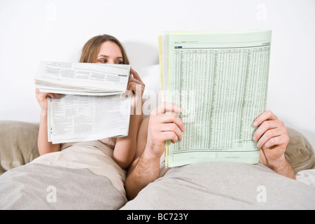 Couple reading newspaper in bed Banque D'Images