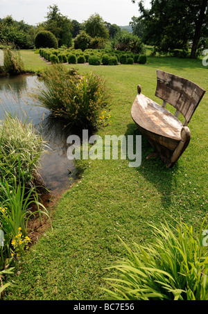 Siège en forme de bateau par le lac d'un jardin anglais aménagé en parc Swan Mews, Somerset, UK Banque D'Images