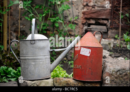 Un vieux gerry rouge huile peut et old fashioned arrosoir dans un jardin Banque D'Images