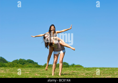 Portrait horizontal de deux adolescentes s'amusant ayant un piggy back ride dans un parc par une belle journée ensoleillée Banque D'Images