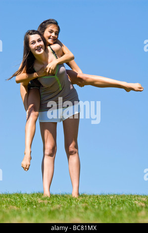 Portrait vertical de deux soeurs à l'extérieur ayant un piggy back ride sur une journée ensoleillée Banque D'Images