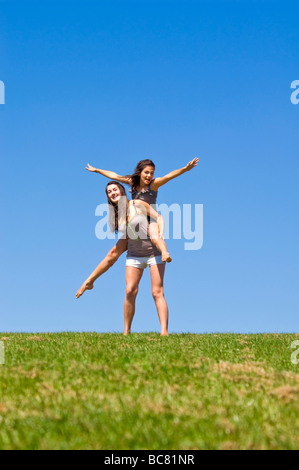 Portrait vertical de deux soeurs à l'extérieur ayant un piggy back ride sur une journée ensoleillée Banque D'Images