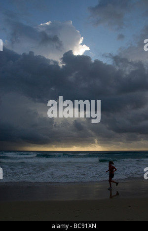 Woman running on beach, tôt le matin, sous les nuages de tempête tropicale, Burleigh Heads, Surfers Paradise, Queensland, Australie Banque D'Images