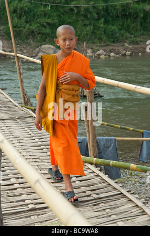 Un jeune novice moine bouddhiste faisant son chemin à travers un pont de bambou sur la rivière Nam Khan à Luang Prabang au Laos Banque D'Images