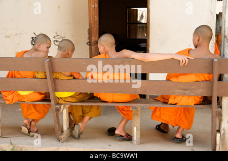 Quatre moines novices se détendre sur un banc après leur scolarité à Luang Prabang au Laos Banque D'Images