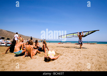 Homme portant une voile de planche à voile beach, groupe de jeune femme à le regarder, Prassionisi Prassionisi, Plage, Rhodes, Grèce Banque D'Images