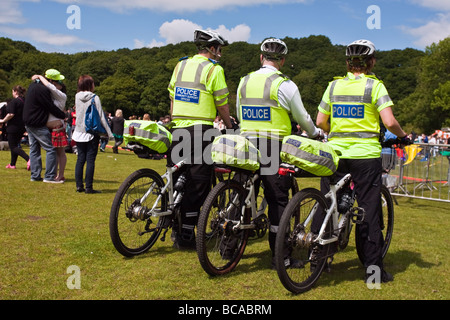 Trois policiers à vélo regarder la foule lors de la gay pride à Sheffield tandis qu'un couple kiss Banque D'Images