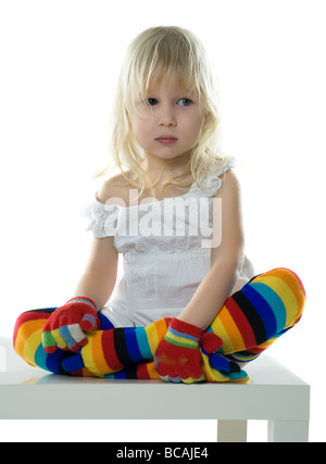 Petite fille en robe blanche multicolore bas et gants de couleur est assis sur chaise blanche Banque D'Images