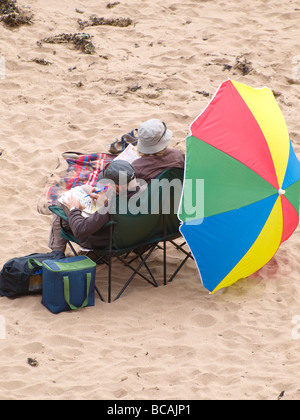 Vieux couple à la plage avec grand parasol faisant des mots croisés Banque D'Images