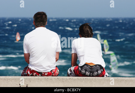 Deux personnes assises sur le mur regarder les véliplanchistes dans Pozo Izquierdo sur Gran Canaria dans les îles Canaries Banque D'Images