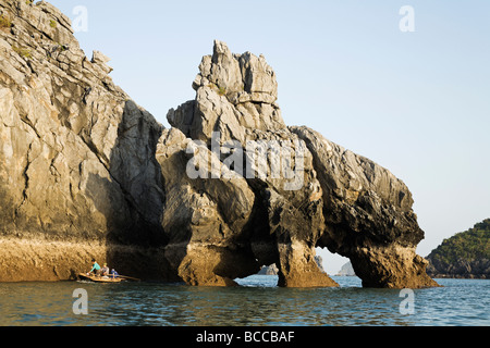 Les pêcheurs locaux dans la baie d'Halong l'aviron au-delà d'un arc double sur une île au sud-ouest de la ville de Cat Ba Banque D'Images