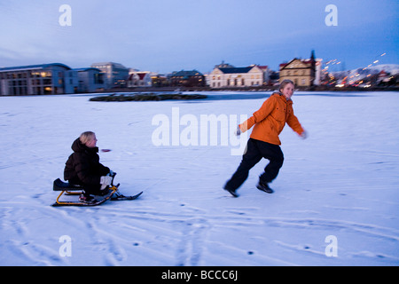 Deux jeunes filles, jouant sur un traîneau neige sur un lac gelé du centre-ville de Tjornin Reykjavik Islande