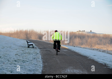 Cyclist riding bike sur la route couverte de neige dans la région de Herrington Country Park, Sunderland, en Angleterre. Banque D'Images