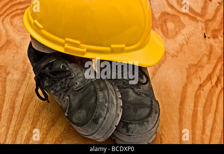 Casque jaune sur le dessus d'une paire de chaussures de travail sale épais Banque D'Images