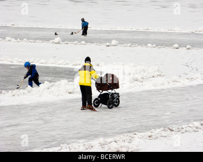 Femme avec les patins en poussant un perambulator sur un lac en Suède. Les enfants jouaient au hockey dans l'arrière-plan. Banque D'Images