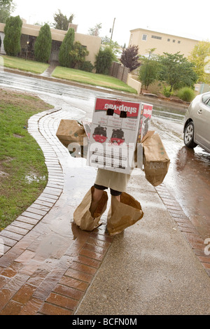 Enfant portant costume fait maison de boîtes et sacs en papier, une marche sous la pluie Banque D'Images