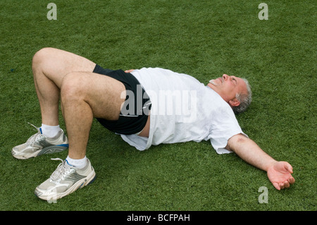 L'excès de l'âge moyen à la retraite et senior homme étend son dos muscles après l'exercice sur un terrain de sport en plein air Banque D'Images