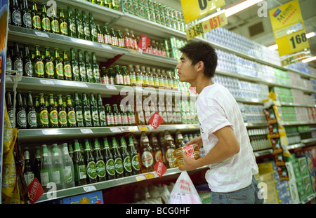 Chinese man shopping au comptoir à bière supermarché Tesco à Beijing, Chine. 2009 Banque D'Images