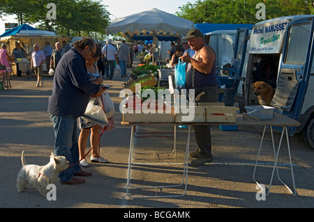 Un couple avec un petit chien blanc achetez des légumes d'un commerçant du marché qui a un plus grand chien regardant le petit chien Banque D'Images