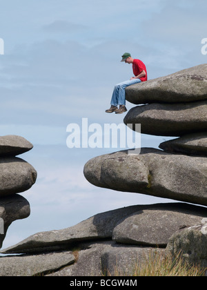 Adolescent assis sur des rochers sur le bord de la carrière de Cheesewring Cornwall Bodmin Moor Banque D'Images