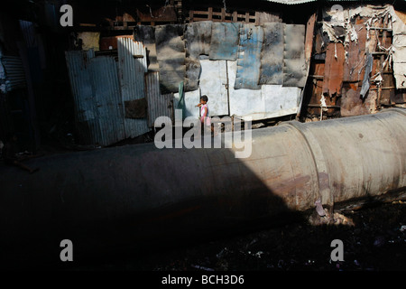 Une jeune fille marche sur un grand tuyau d'eau qui est utilisée comme une rue dans le pauvre bidonville de Dharavi à Mumbai (Bombay) en Inde. Banque D'Images