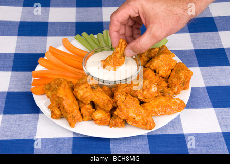 Un plat de poulet hot wings le céleri et les carottes avec sauce attire un homme qui plonge une aile dans une sauce ranch savoureux Banque D'Images