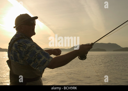 Pêche à la mouche l'homme rive de la baie Sitka SE AK de l'été près de Harbour Pt Silhouette Banque D'Images