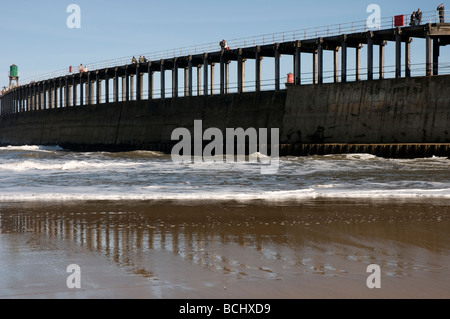 Les promeneurs sur le mur du port vue de la plage à Whitby, dans le Yorkshire du Nord. Banque D'Images