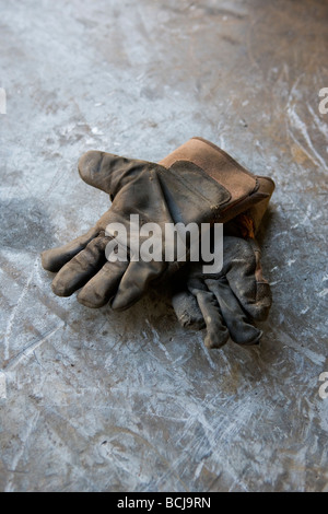 Le vieux cuir usé gants de travail reposant sur la surface métallique Banque D'Images