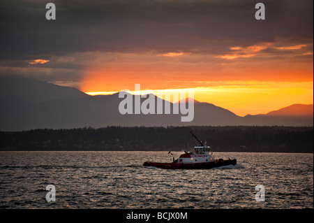 Au coucher du soleil un remorqueur navigue Elliott Bay ce qui rend le chemin de l'accueil c'est à Seattle, Washington. Montagnes Olympiques dans le contexte Banque D'Images