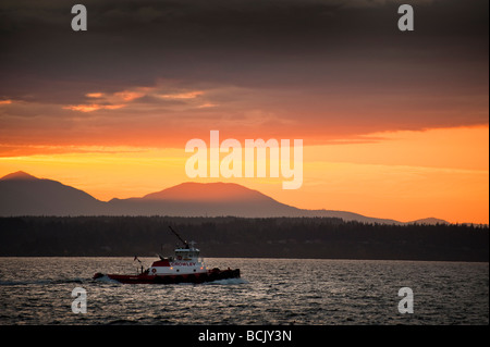 Au coucher du soleil un remorqueur navigue Elliott Bay ce qui rend le chemin de l'accueil c'est à Seattle, Washington. Montagnes Olympiques dans le contexte Banque D'Images