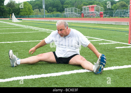 L'excès de l'âge moyen à la retraite et senior man stretching les muscles des jambes après s'exercer sur un terrain de sport en plein air Banque D'Images