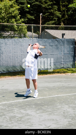 L'âge moyen beau joueur de tennis masculin servant avec balle en l'air sur de tennis au club Banque D'Images