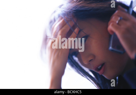 Woman holding head talking on cell phone Banque D'Images