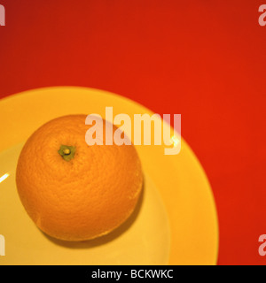 Orange sur la plaque jaune sur fond rouge, overhead view Banque D'Images