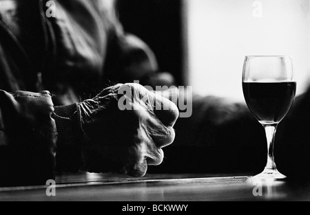 Personne âgée main sur table avec verre de vin, b&w Banque D'Images