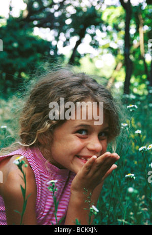 Girl sitting in grass, smiling, main devant la bouche Banque D'Images