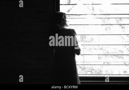 Femme debout, à la fenêtre de sortie, b&w Banque D'Images