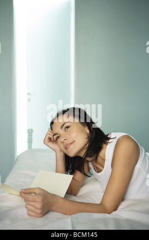 Woman lying on bed with lettre, daydreaming Banque D'Images