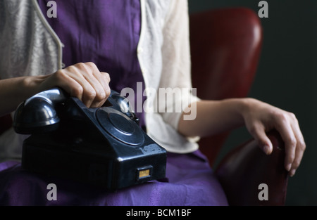 Woman in dress sitting avec téléphone sur les genoux, la main sur le récepteur, cropped view of mid section Banque D'Images