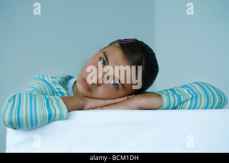 Preteen girl resting head on arms, looking at camera Banque D'Images