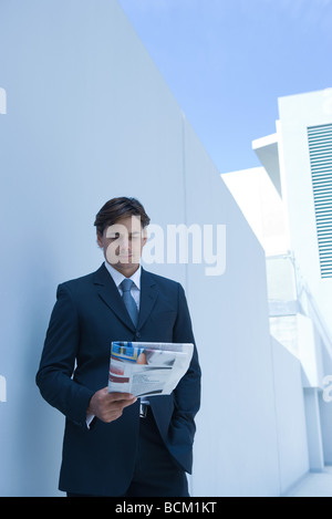 Businessman standing outdoors, reading newspaper Banque D'Images