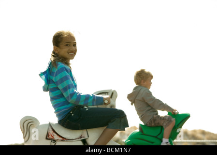 Les enfants équitation chevaux à bascule sur l'aire de jeux, l'accent sur le premier plan Banque D'Images