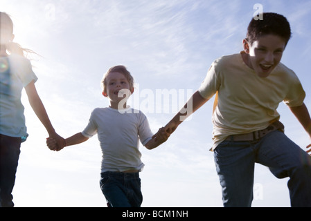 Trois enfants en marche, se tenant la main et riant, low angle view Banque D'Images