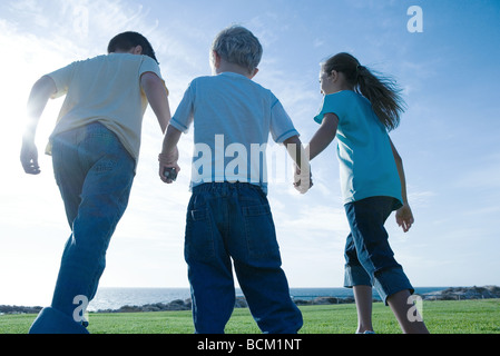 Trois enfants marchant sur l'herbe, tenant les mains, low angle view Banque D'Images