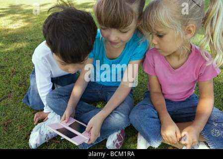 Trois enfants assis sur l'herbe, jouer avec des jeux vidéo, close-up Banque D'Images