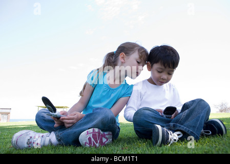 Fille et garçon détenant tous les téléphones cellulaires, la fille se penche au-dessus de regarder le téléphone de garçon Banque D'Images