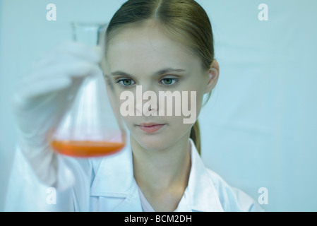 Female scientist holding up bécher avec liquide à l'intérieur, regardant vers le bas, close-up Banque D'Images