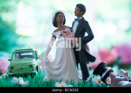 Bride and Groom figurines posant dans le champ de fleurs faux, main tenir l'appareil photo en premier plan Banque D'Images